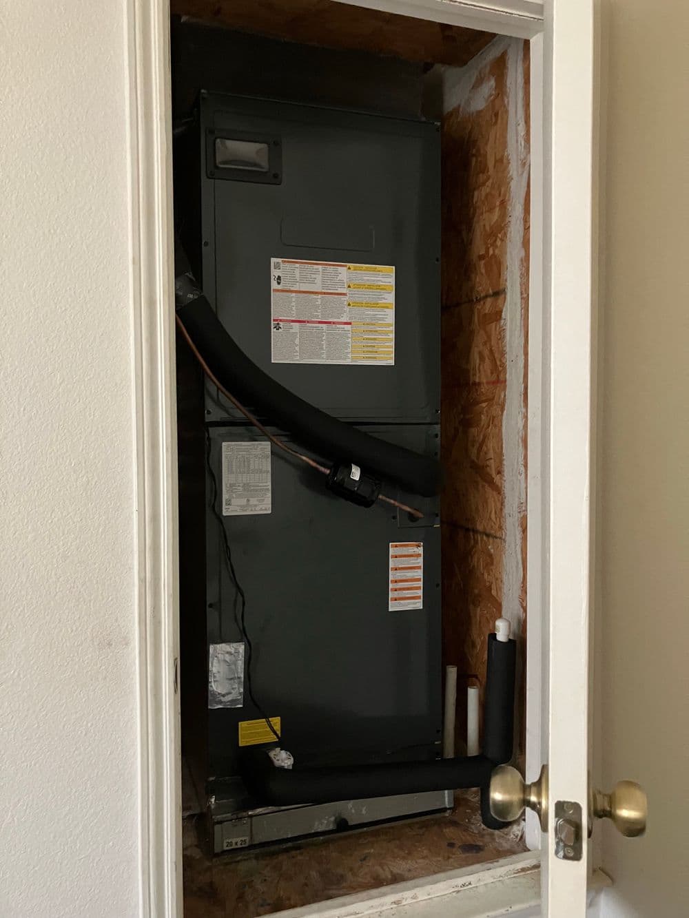 Furnace installed in a closet, featuring safety labels and connected ductwork.