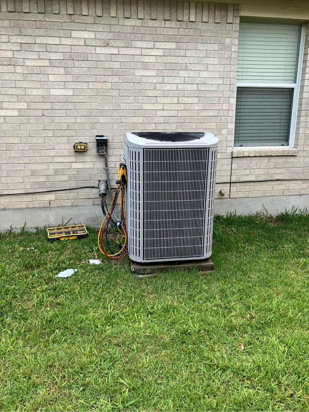 Air conditioning unit installed outside a brick house on a grassy area.