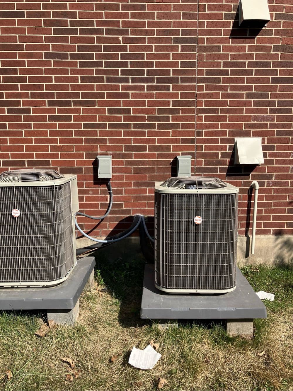 Two air conditioning units beside a brick wall, with electrical connections visible.