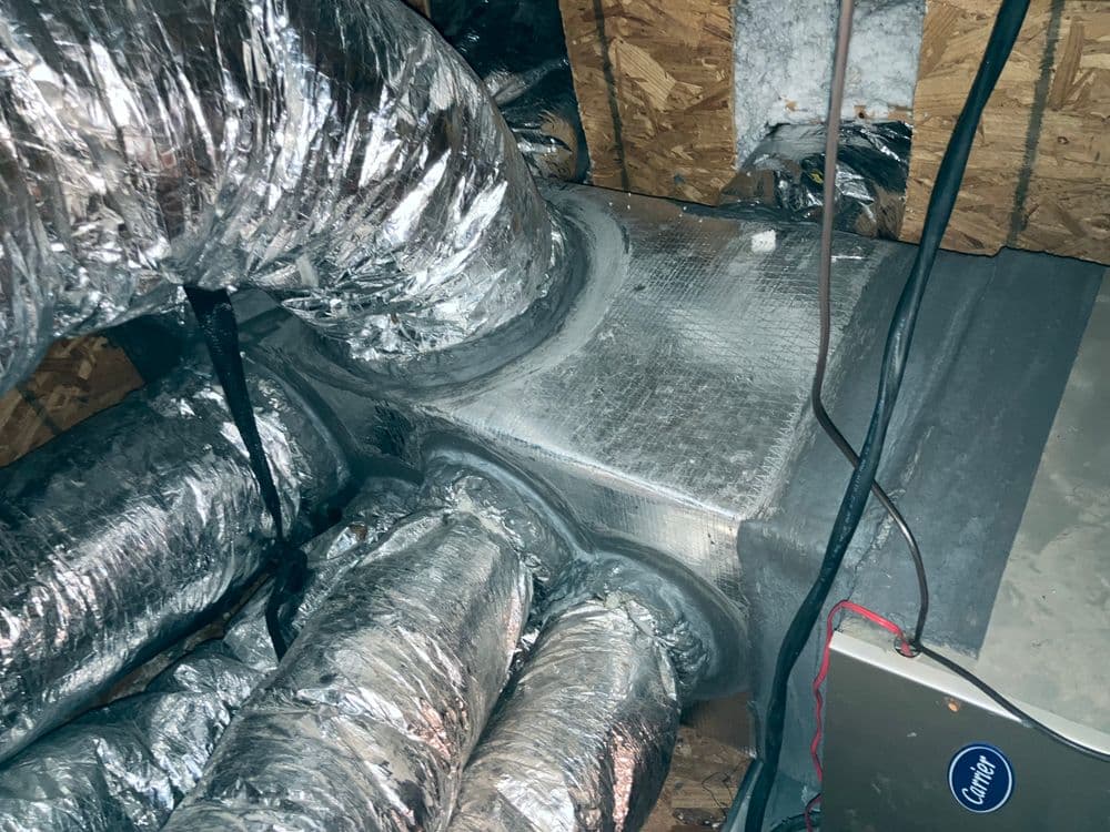 Ductwork in attic with insulated silver tubing and HVAC equipment visible.
