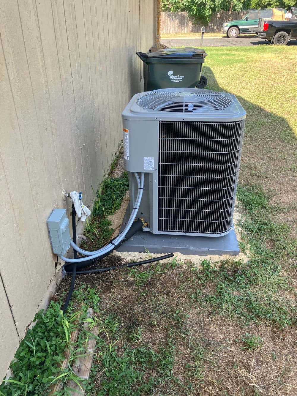 Air conditioning unit installed beside a house, with electrical and drainage connections visible.