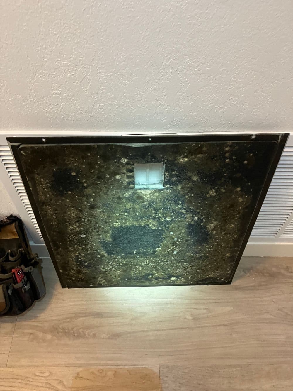 Dirty metal panel with a vent opening, resting on a wooden floor near tools and equipment.