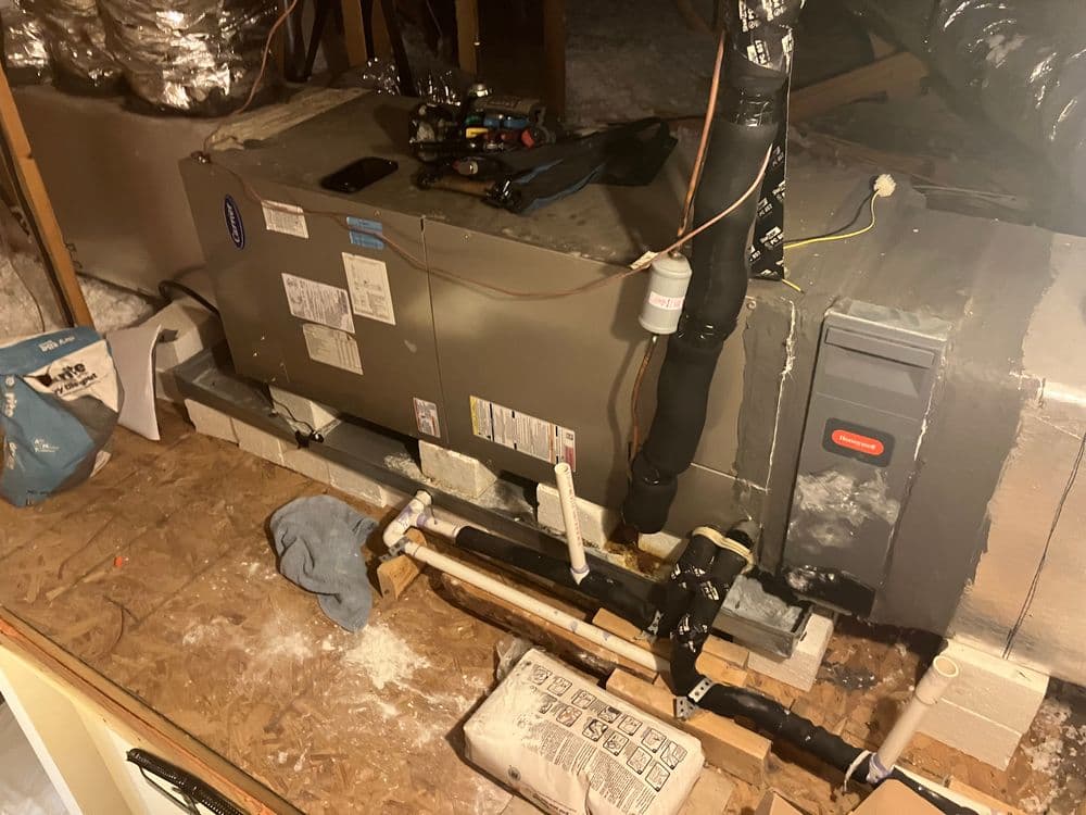 Air conditioning unit in an attic with pipes and tools, showcasing HVAC installation setup.