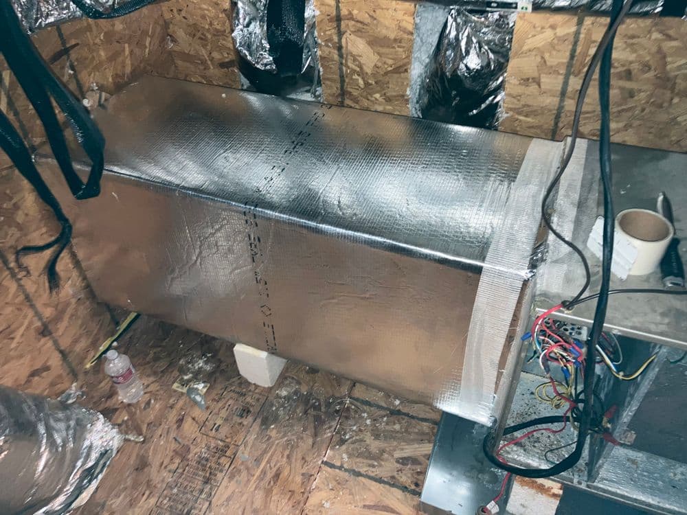 Insulated HVAC unit in a basement, surrounded by ductwork and electrical wiring.