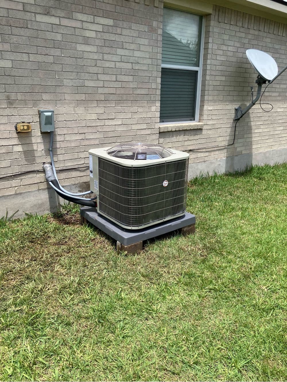 Outdoor central air conditioning unit installed next to a house, on grassy ground.