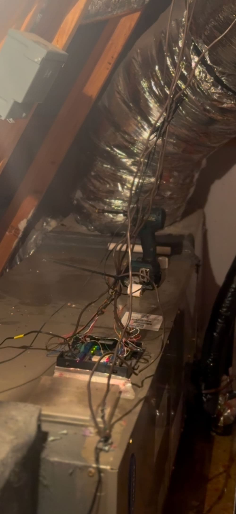 Wires and tools cluttered on a workbench in an attic space, showcasing DIY project setup.