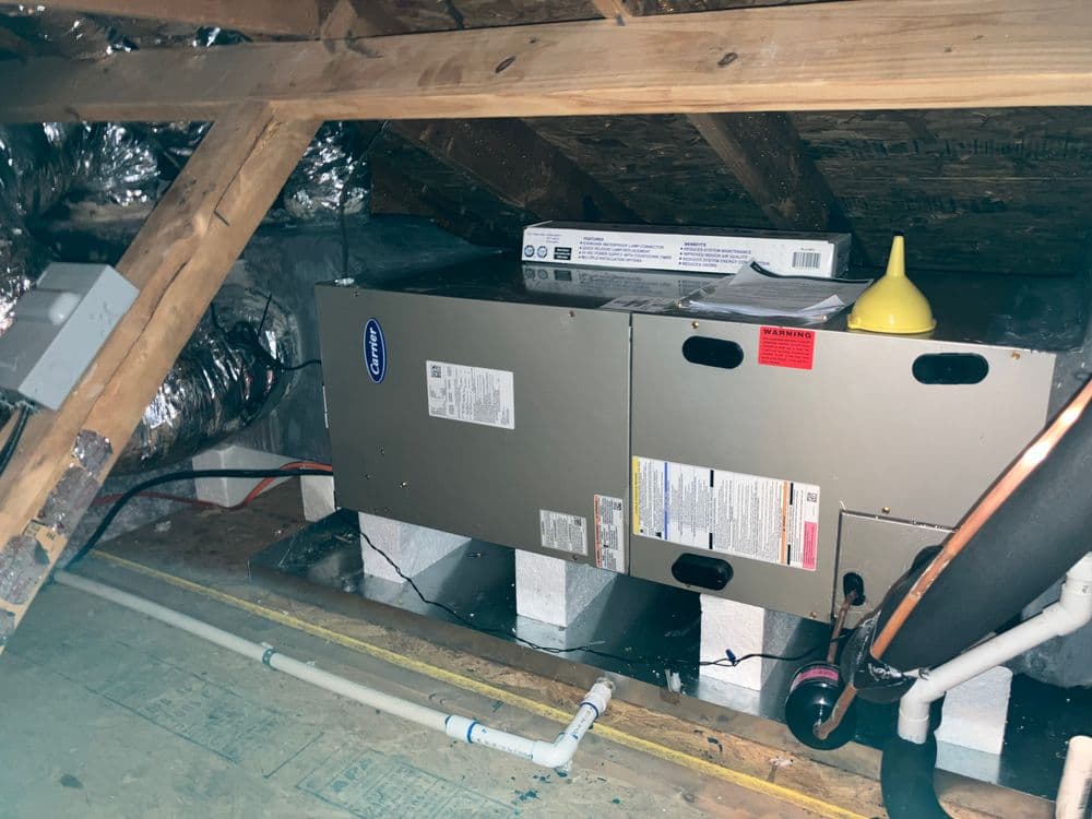 Heating and cooling unit installed in an attic with ventilation ducts and a funnel nearby.