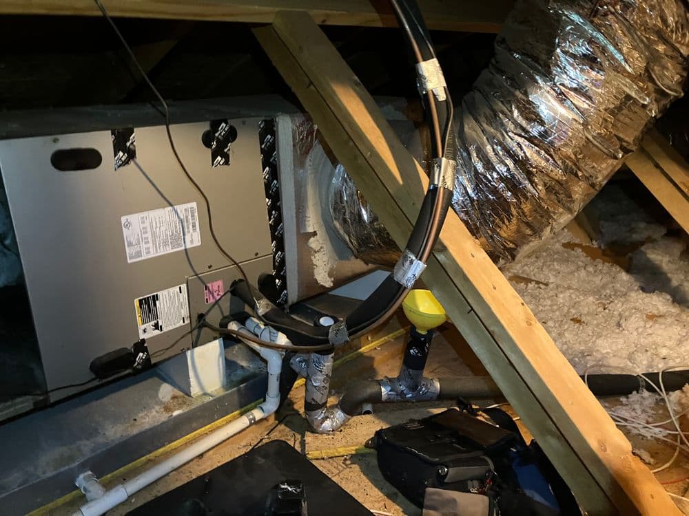HVAC system in attic with ductwork and piping, insulation visible, well-lit installation space.